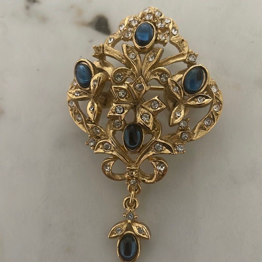 Goldtone filagree brooch with sapphire color/rhinestone detail.